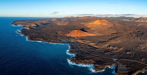 Coast with lava fields, volcanic landscape near Los Hervideros with red volcano Montaña Bermeja, in