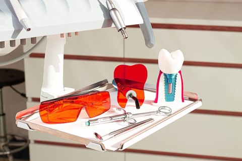 On the tray are various dental instruments, a model dental implant and bright orange safety