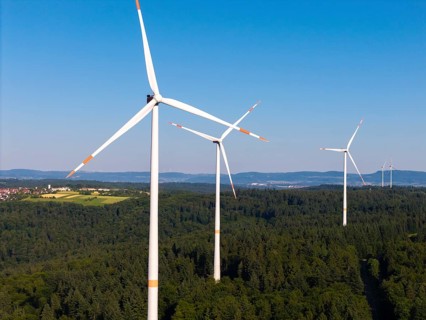 Three wind turbines rise above a green forest under a clear sky, near Schorndorf, Remstal,