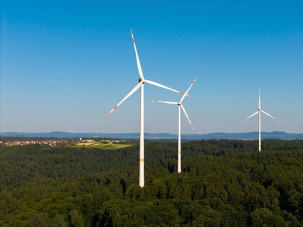 Three wind turbines above a dense forest area under a clear sky, near Schorndorf, Remstal,