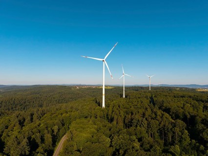 A series of wind turbines on a wooded hill under a wide blue sky, near Schorndorf, Remstal,