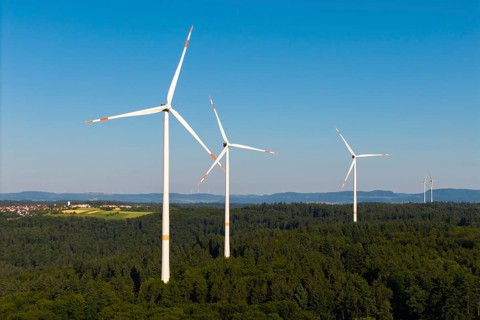 Wind turbines stand in a wooded landscape under a wide blue sky, near Schorndorf, Remstal,