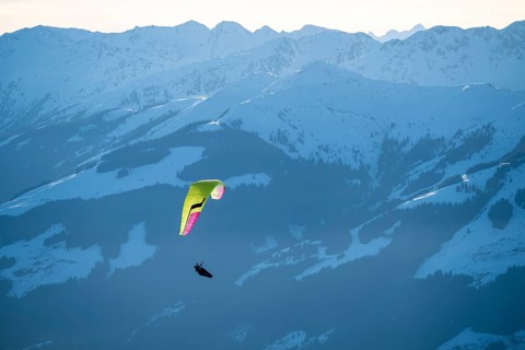 Paragliders flying over snowy mountain peaks in winter in evening light, Kitzbühel Alps, Tyrol,