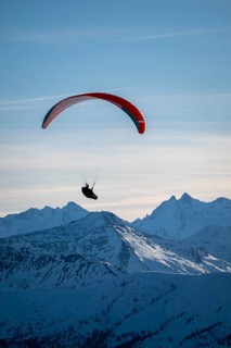 Paragliders flying over snowy mountain peaks in winter in evening light, Kitzbühel Alps, Tyrol,