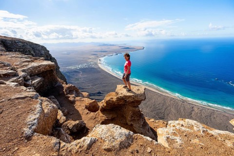 Woman enjoying the view from the Risco de Famara cliffs on Famara beach, Playa de Famara with La