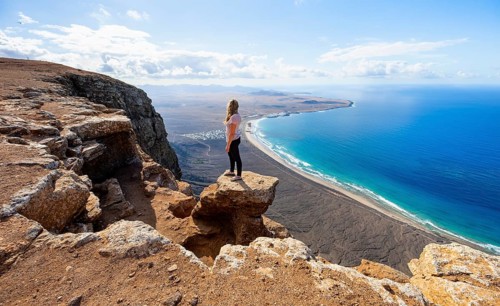 Young woman enjoying the view from the Risco de Famara cliffs to Famara beach, Playa de Famara with