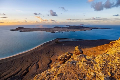 View of steep cliffs to sea and the island of La Graciosa, Mirador del Porrito viewpoint at sunset,