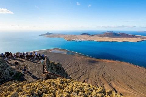 View of La Graciosa island with volcanic craters in the evening light, tourists on an observation