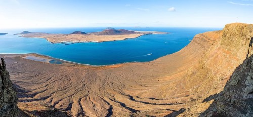 View of steep cliffs by the sea and island of La Graciosa with volcanic craters in the evening