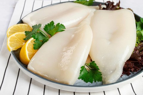 Fresh squid on a black plate with greens and lemon slices prepared for cooking in a kitchen setting