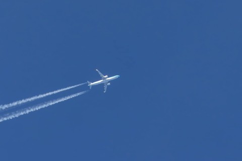 Jet passenger aircraft flying in a blue sky with contrails or vapour trails behind, England, United