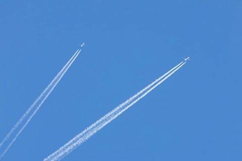 Two jet passenger aircraft flying in a blue sky with contrails or vapour trails behind, England,