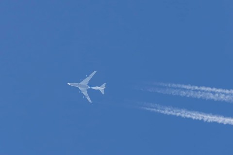 Boeing 747 jumbo jet cargo aircraft flying in a blue sky with contrails or vapour trails behind,