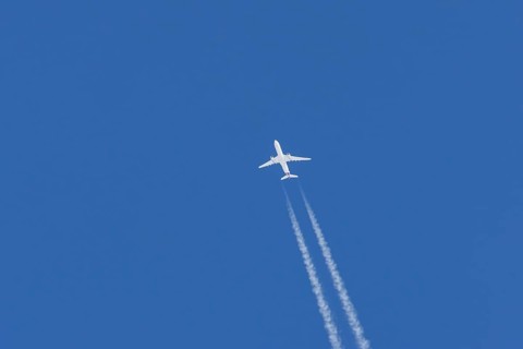 Jet passenger aircraft flying in a blue sky with contrails or vapour trails behind, England, United