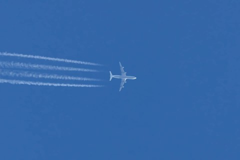 Jet commercial passenger aircraft flying in a blue sky with contrails or vapour trails behind,