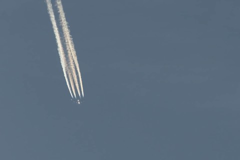 Jet passenger aircraft flying in a blue sky with contrails or vapour trails behind, England, United