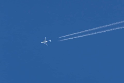 Airbus jet passenger aircraft flying in a blue sky with contrails or vapour trails behind, England,