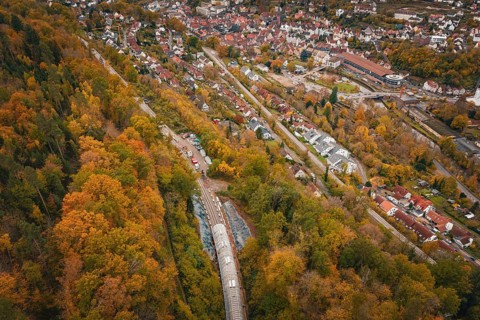 Aerial view of a city next to an autumnal forest landscape with train tunnel, Hermann-Hesse-Bahn