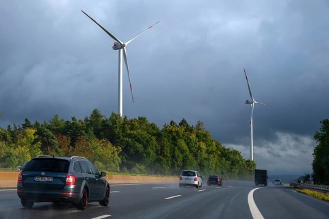 Tourist traffic on the A9 motorway during thunderstorms, wind turbines in the pine forest in the