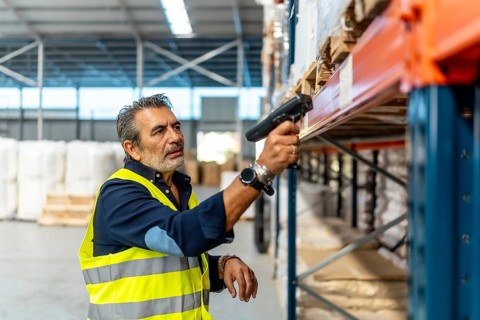 Mature man wearing a safety vest scanning barcodes on shelves with a handheld scanner, managing
