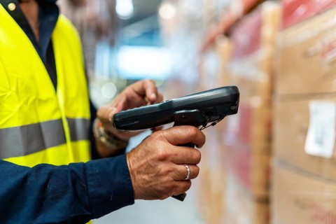 Warehouse worker in high visibility vest and blue uniform scanning barcodes on boxes with handheld