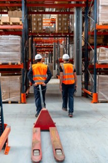 Warehouse workers in safety vests and hard hats navigating through industrial shelving with a