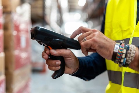 Warehouse worker in high visibility vest holding a barcode scanner, efficiently managing inventory