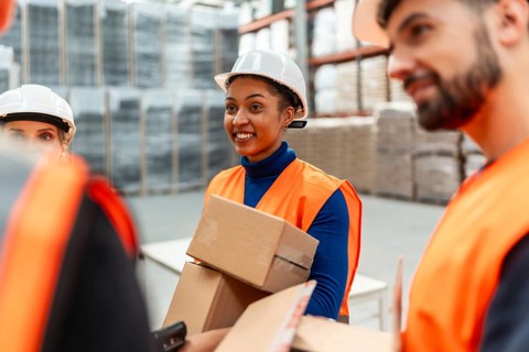 Diverse team of logistics workers wearing safety vests and hard hats, collaborating on picking and