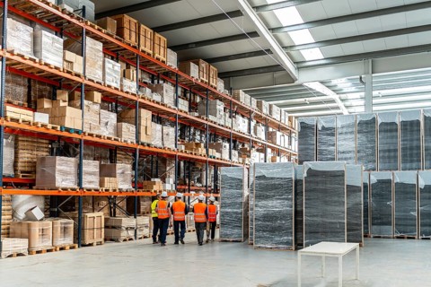 Logistics team in hard hats and hi vis vests walking through a bright industrial warehouse,