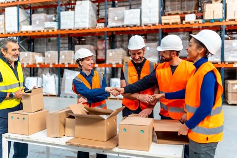 Diverse group of logistics workers shaking hands in a busy distribution warehouse, celebrating a