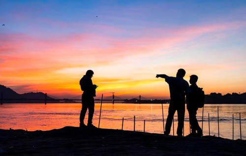 People enjoy the vibrant sunset by the Brahmaputra riverside, capturing photos and moments against