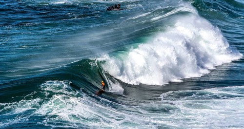 Surfers with their jet ski pilots in the Atlantic waves below Farol de Nazaré, Forte São Miguel,