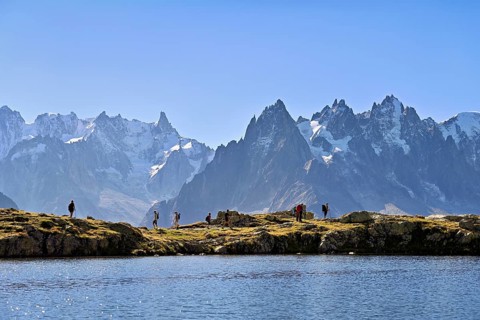 A group of hikers at Lac de Chésserys, behind the snow-covered Mont Blanc massif,