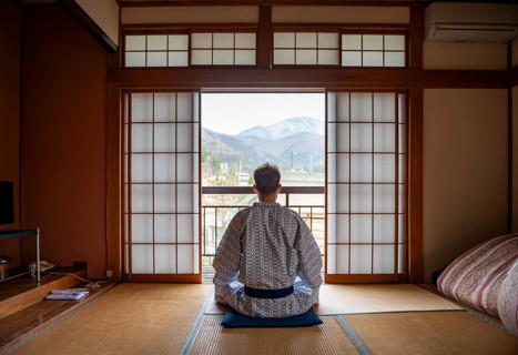 Young man wearing kimono sitting in traditional Japanese living room with tatami mats and shoji