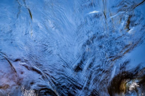 Shimmering blue water surface of a stream, current, light reflections, abstraction, long exposure,