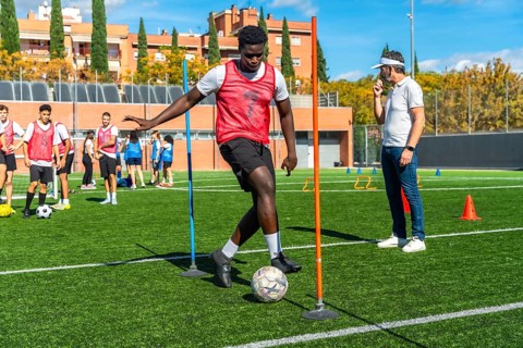 Young soccer player dribbling a football through slalom poles during an outdoor training session on