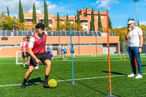 Young male student athlete concentrating on dribbling a soccer ball between poles during a drills
