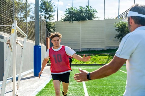 Youth male soccer player in a red bib running towards a coach with outstretched arms, receiving