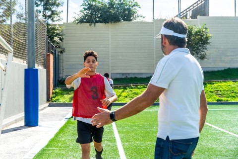 Youth male soccer player in a red bib running towards a male coach with an outstretched hand,