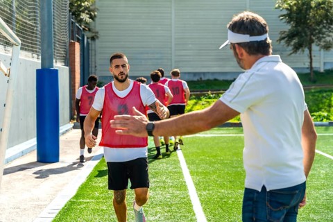 Soccer team players running sprints on a green artificial turf field, receiving an encouraging high