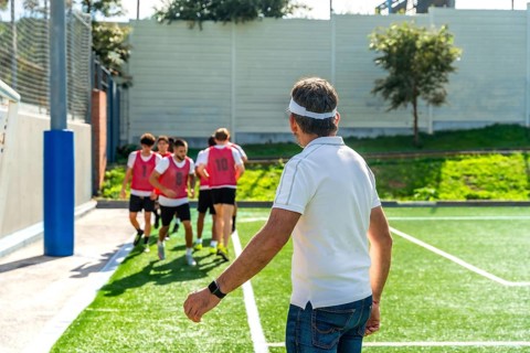 Soccer coach watches youth team warming up on artificial turf, guiding drills and preparation for