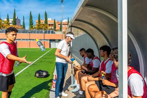 Soccer coach distributing water bottles to young male players resting in the dugout during a