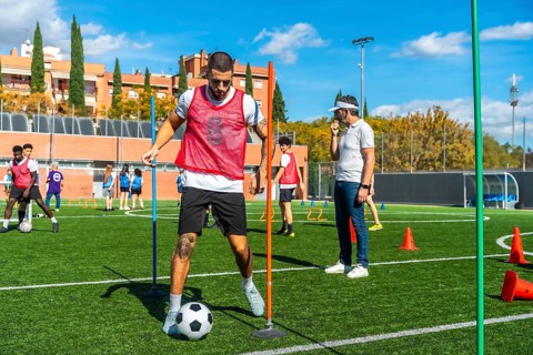 Soccer player is training on a professional artificial turf field, dribbling a ball through
