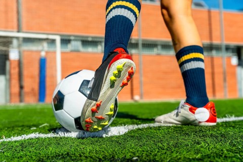 Female soccer player wearing a cleat and blue socks standing with a ball on a green artificial turf