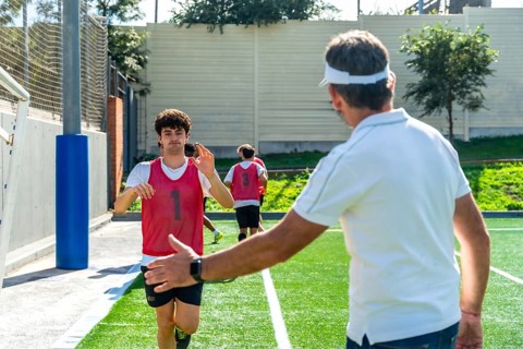 Soccer coach extending hand for a high five with a young male player wearing a red bib during a