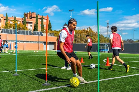 Young man in a red vest training soccer dribbling techniques on a green artificial turf field,