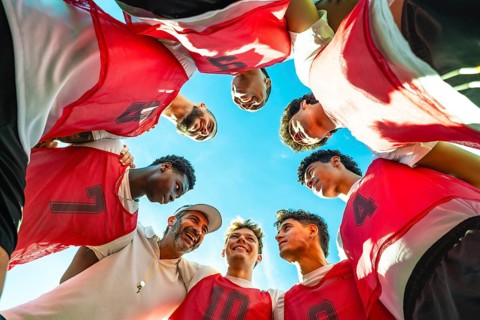 Coach and young diverse male soccer players forming a huddle, discussing strategy and fostering