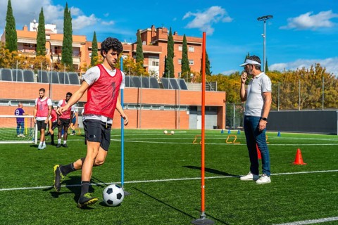 Soccer player training during an agility drill on a green field, dribbling a ball around poles