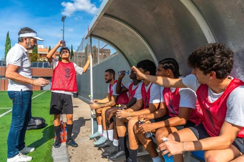 Soccer coach briefing male players on the sideline bench during a break, discussing strategy and