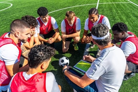 Soccer coach providing strategic instructions to his diverse team of young male players, gathered